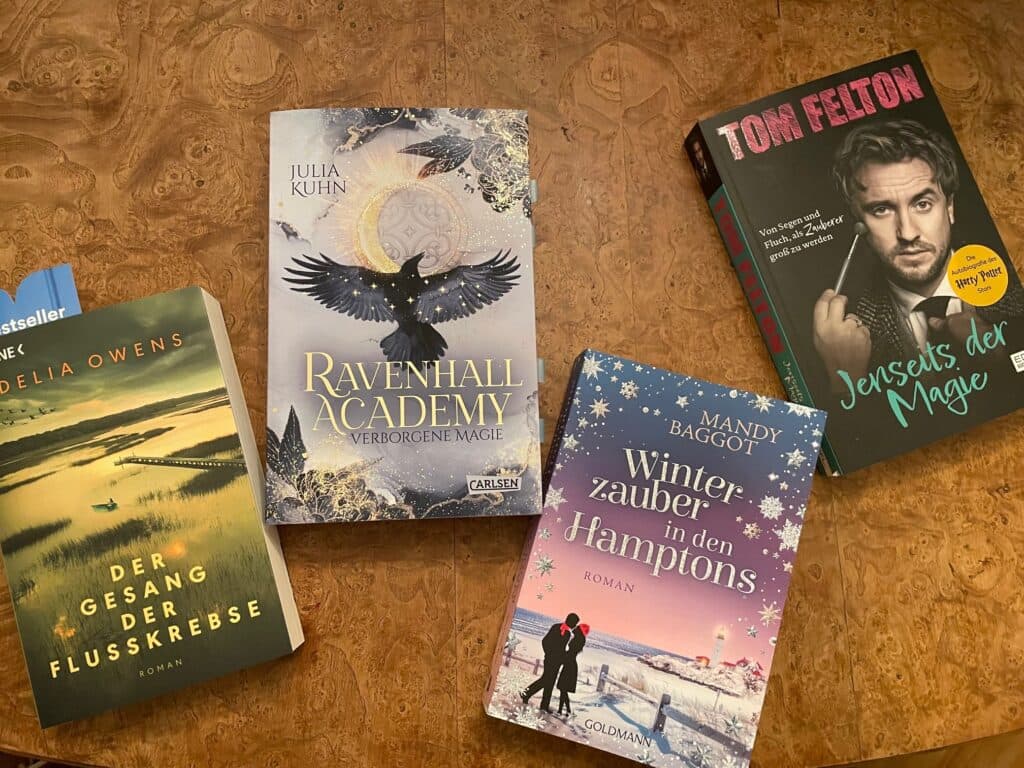 Fünf neue Bücher, darunter "Ravenhall Academy" und "Jenseits der Magie", auf einem Holztisch