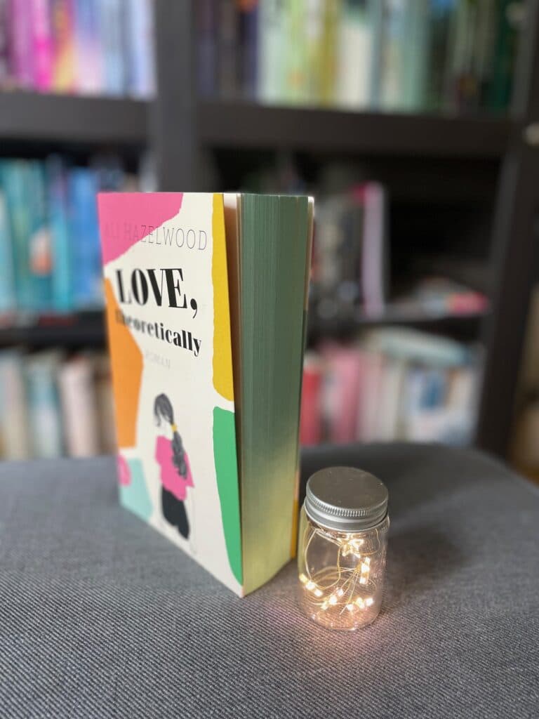 Grüner Buchschnitt von "Love, Theoretically" von Ali Hazelwood neben einem Lichtglas