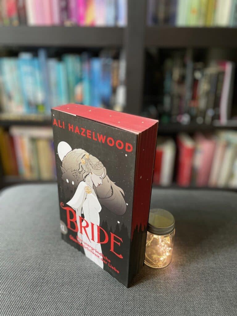 Buch "Bride" von Ali Hazelwood mit rotem Buchschnitt neben einem Lichtglas